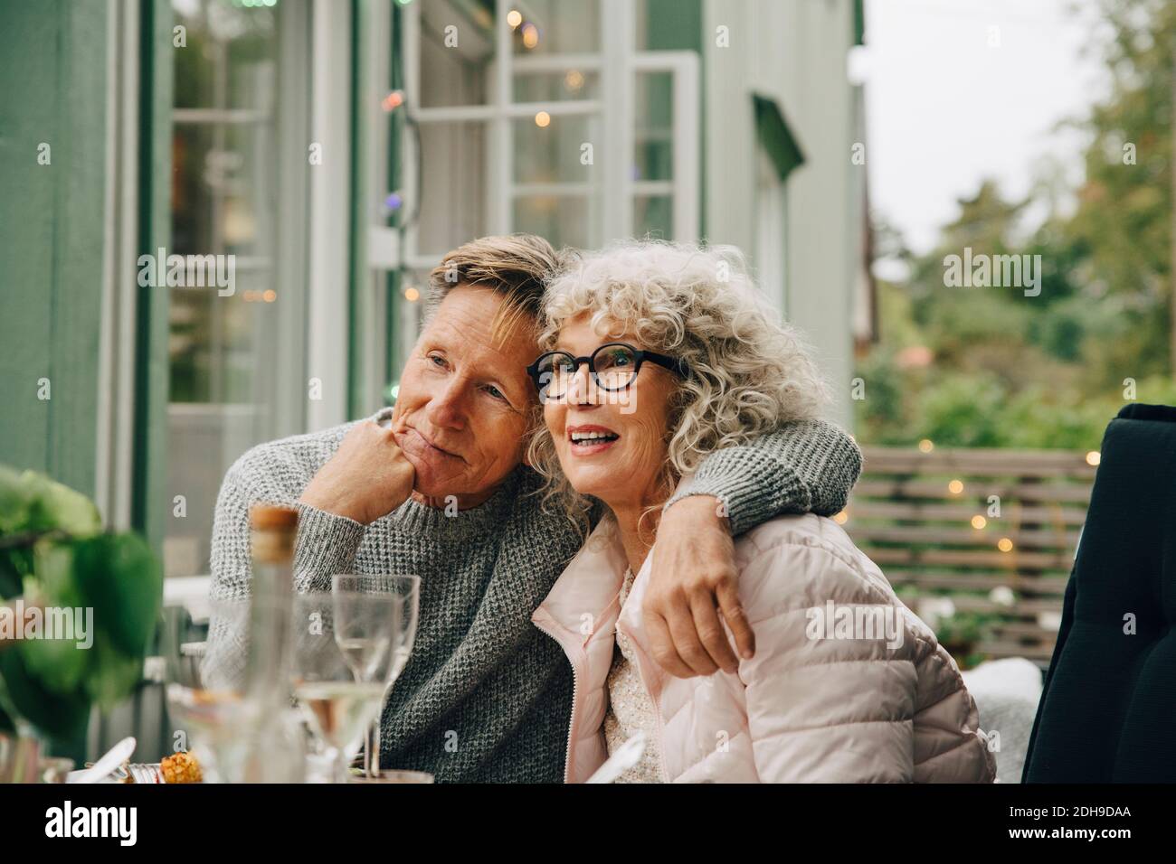 Thoughtful senior man sitting with arm around woman at dining table during garden party Stock Photo