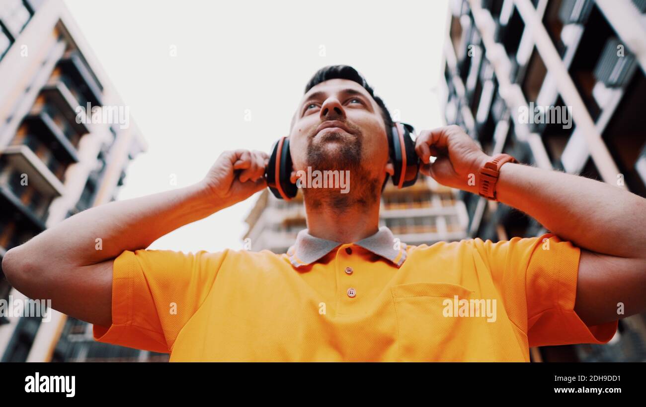 Man wearing safety equipment hearing protection. Worker wearing noise cancelling ear defenders or ear muffs. Construction builde Stock Photo