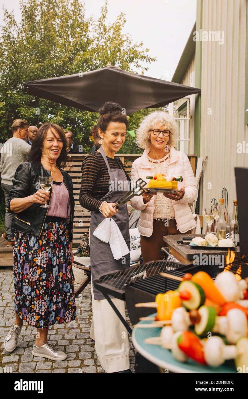 Happy elderly female friends preparing dinner on barbecue at back yard Stock Photo