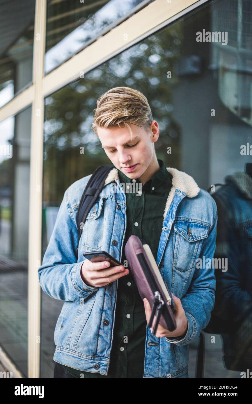 Young man using mobile phone while leaning on glass wall Stock Photo