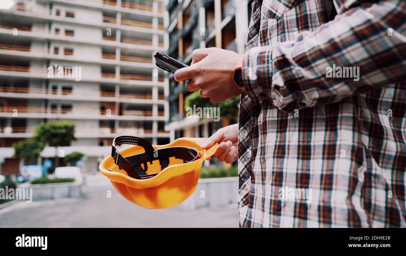 Young Engineer using smartphone on construction site. Architect using phone. Manager development building texting on smart phone Stock Photo