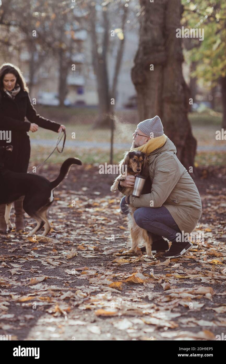Full length of man crouching while embracing dog by woman with pet at park Stock Photo