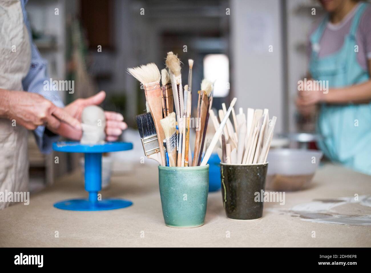 Hand tools and paintbrushes in containers on workbench with female ...