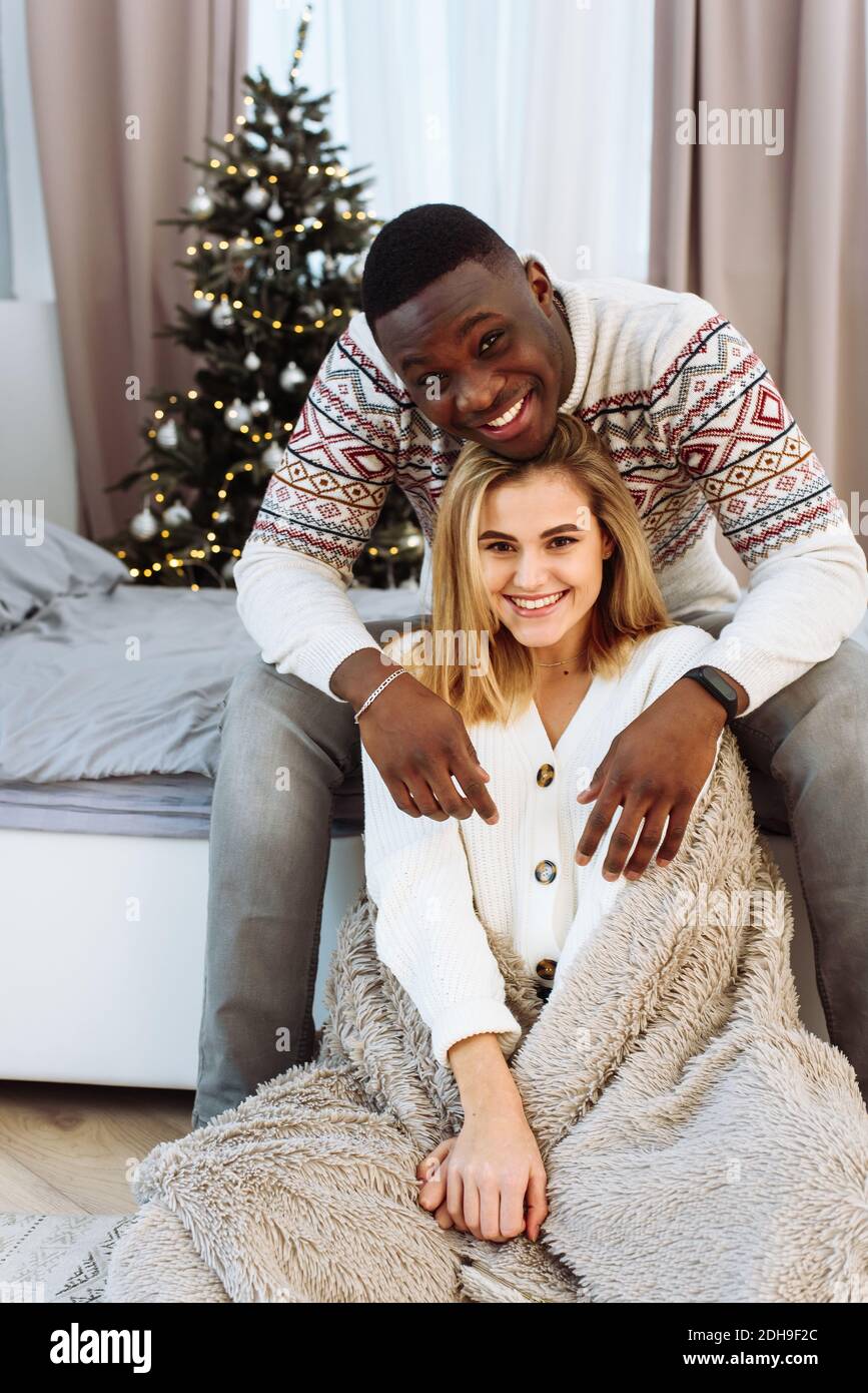 Young happy couple embracing and relaxing on comfortable bed. Lovely  multiethnic couple wearing christmas sweater and hugging. African man and  affecti Stock Photo - Alamy