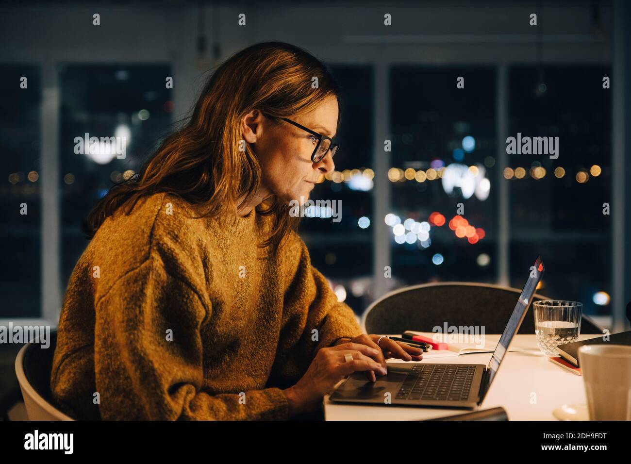 Ambitious businesswoman using laptop while working late at creative office Stock Photo