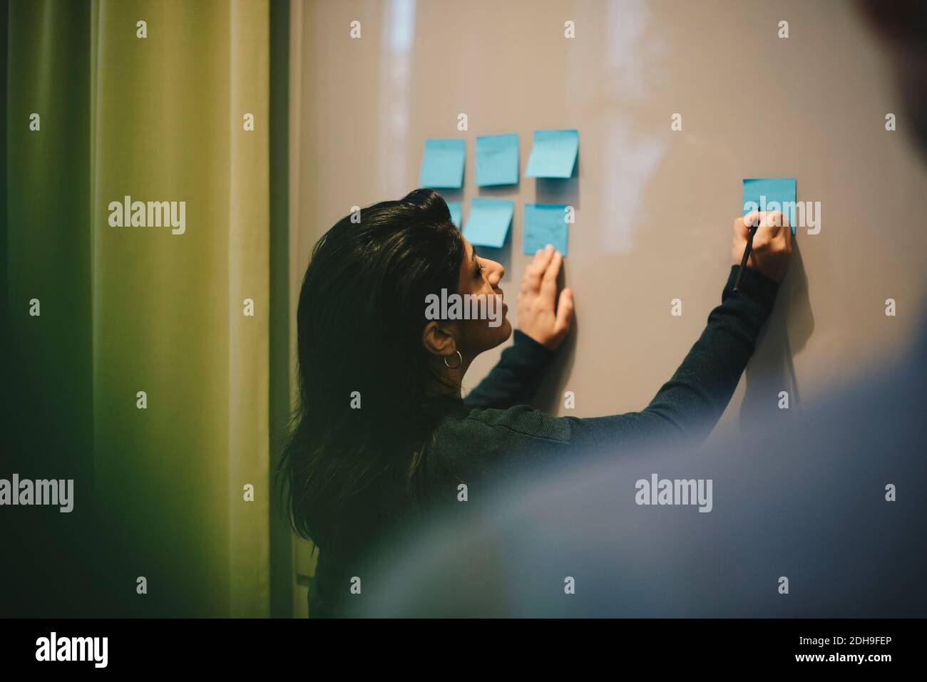 Rear view of businesswoman analyzing adhesive notes stuck on whiteboard in office Stock Photo