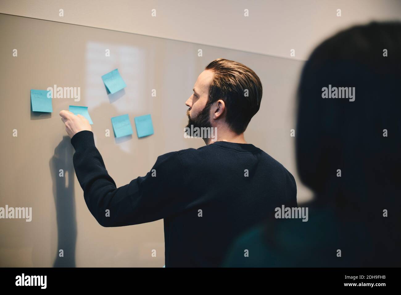 Rear view of businessman explaining plan on adhesive notes to female colleague in office Stock Photo