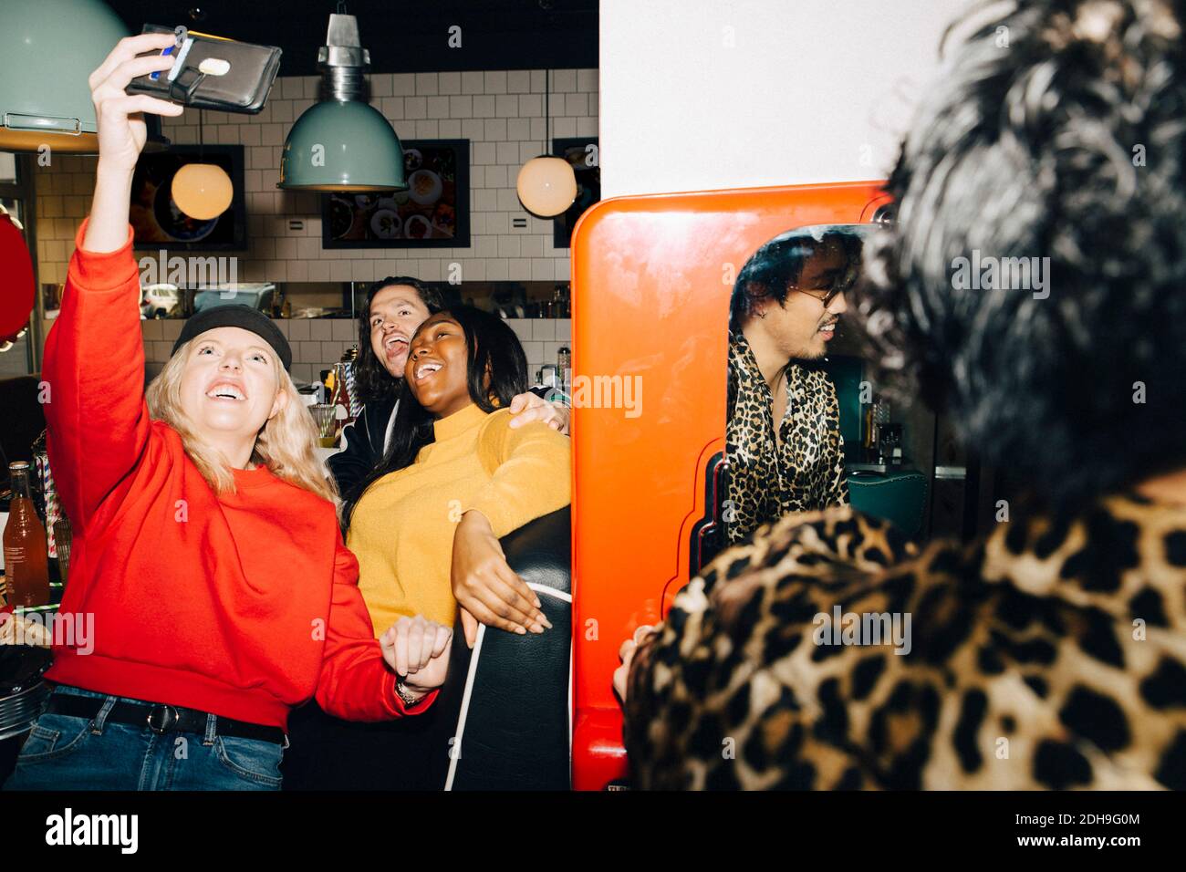 Smiling female taking selfie with friends in cafe Stock Photo