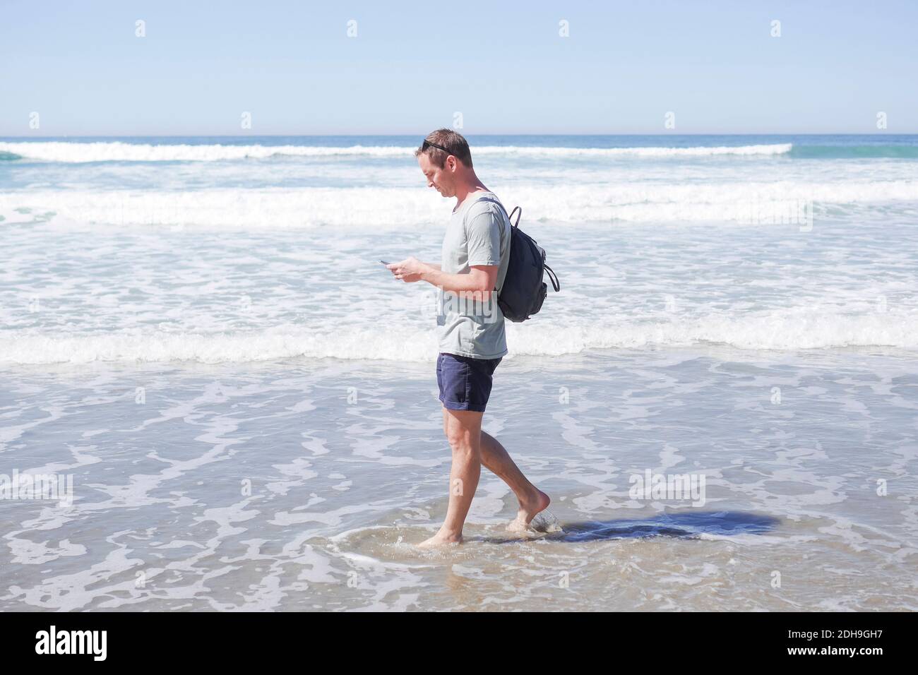 Full length side view of mature man using mobile phone while walking in sea at beach Stock Photo