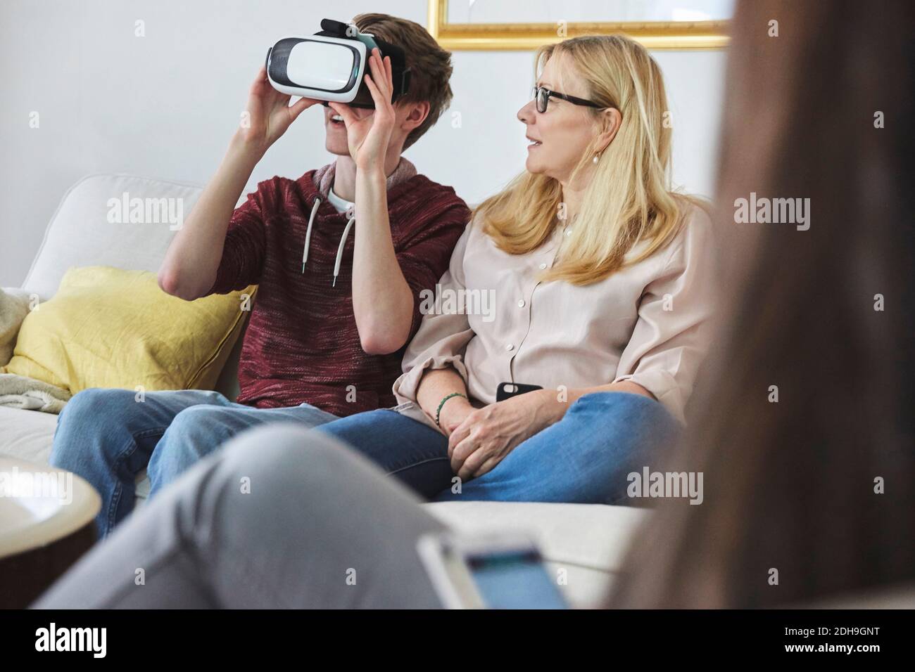 Mother looking at son using virtual reality headset while sitting on sofa Stock Photo
