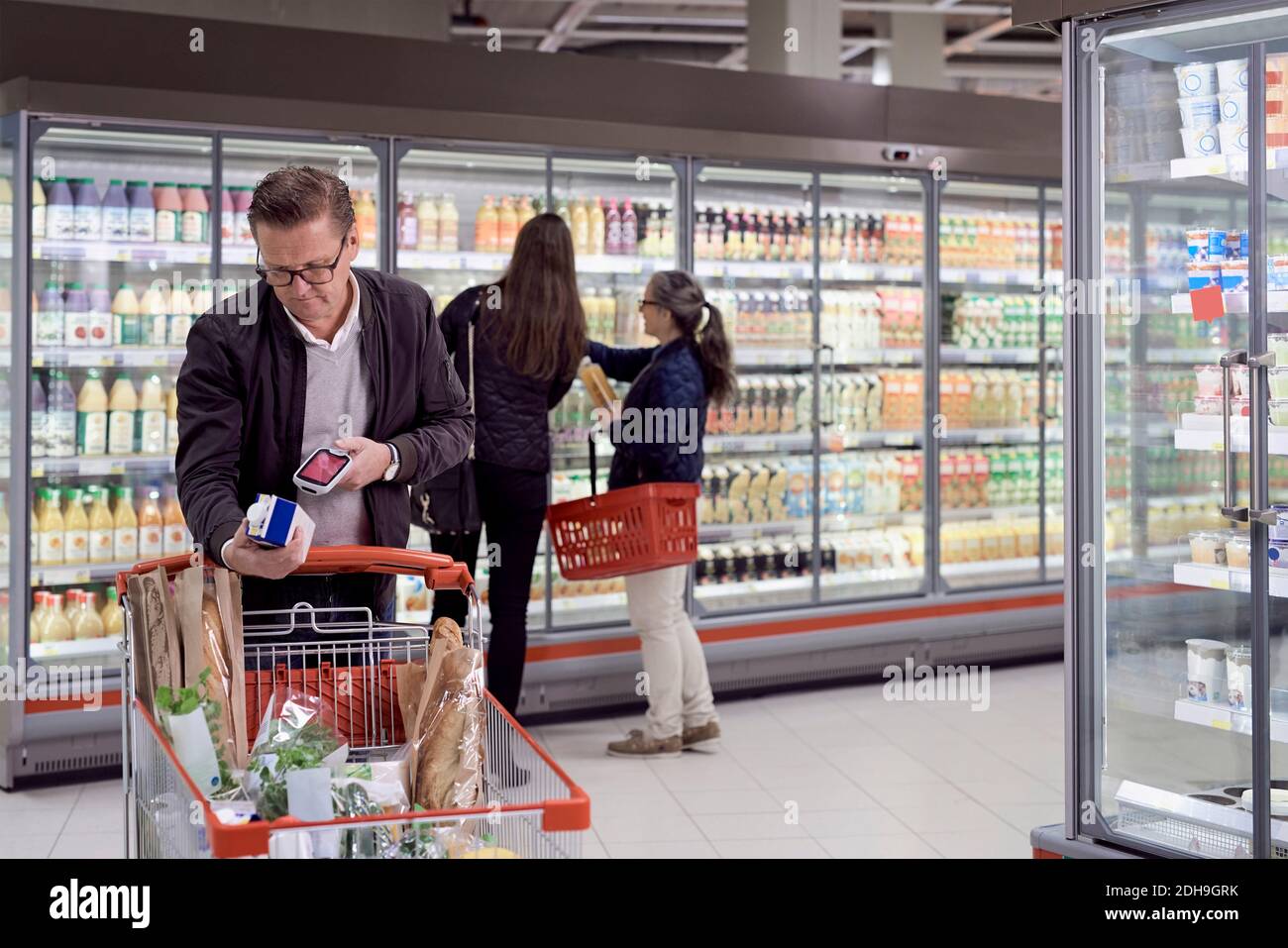 Mature man scanning juice box with reader against women buying at refrigerated section in supermarket Stock Photo