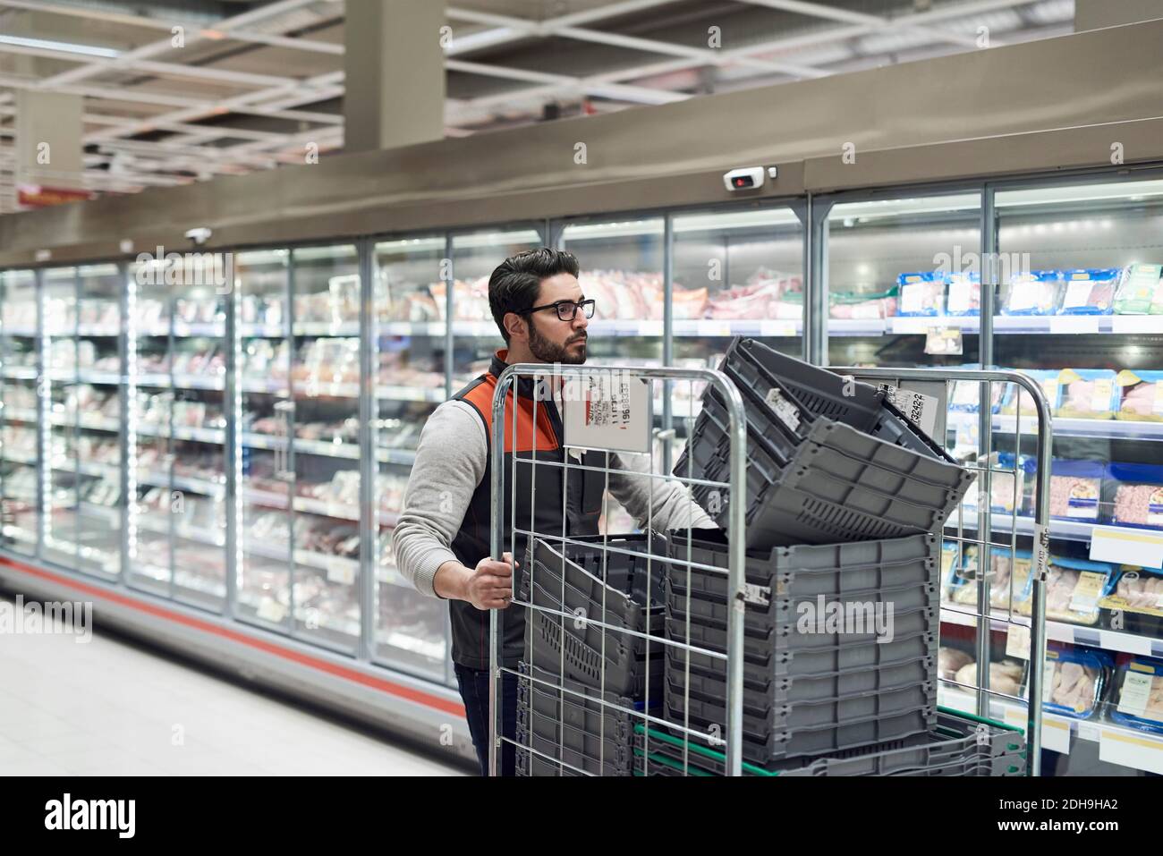 Sales clerk pushing cart with plastic crates at supermarket Stock Photo