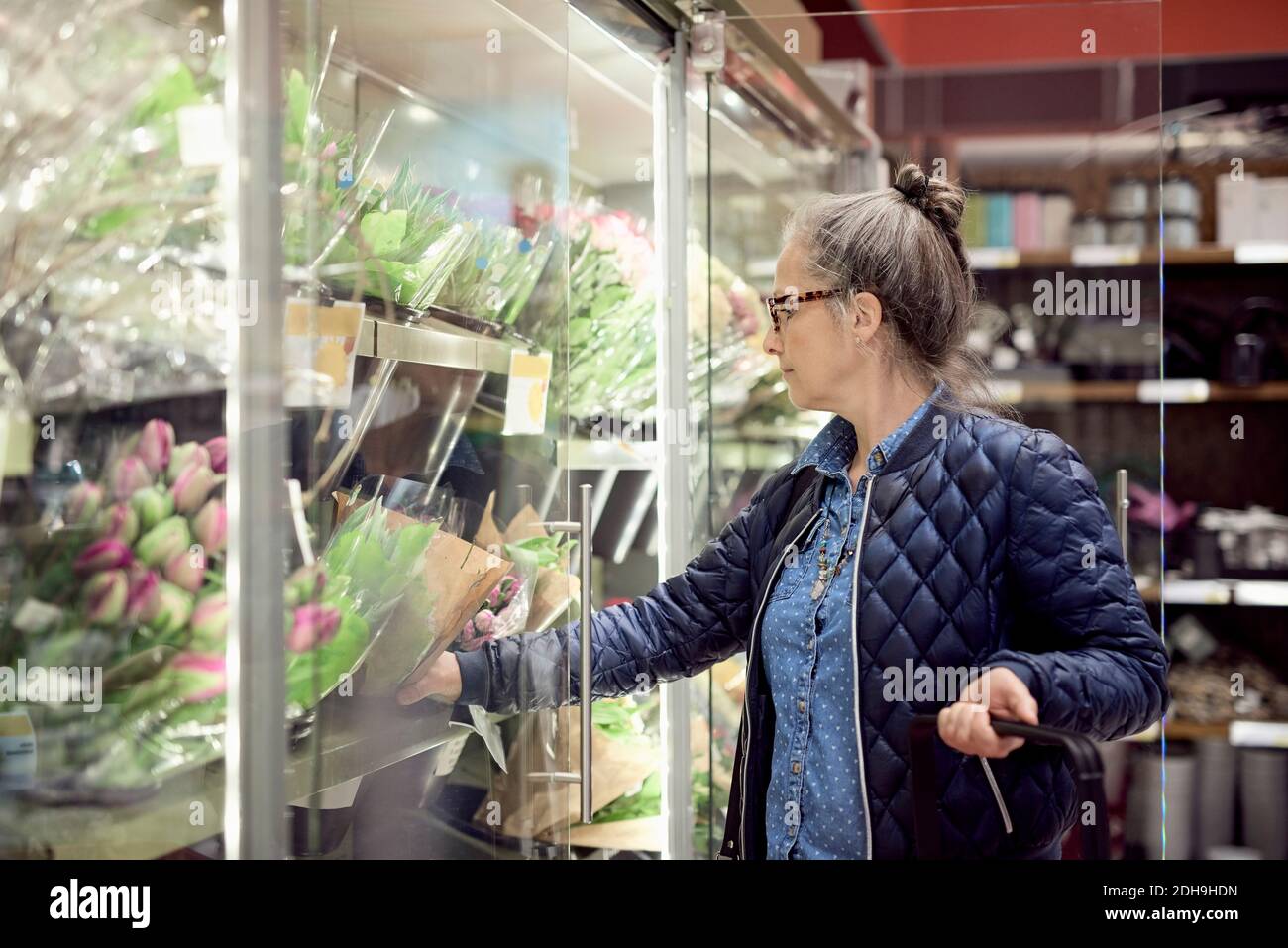Mature woman buying flowers from glass cabinet at supermarket Stock Photo