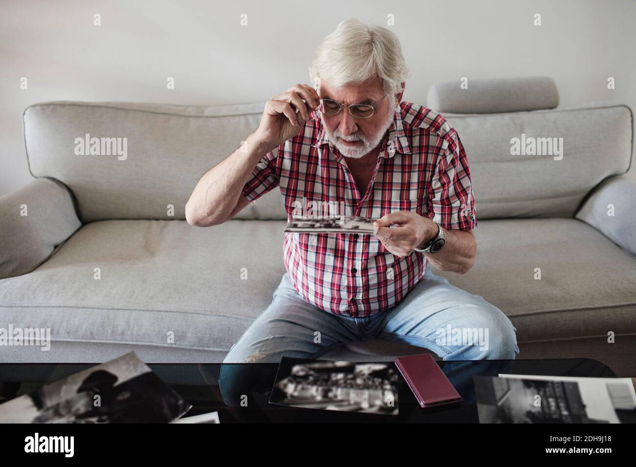 Senior man looking at vintage photographs while sitting on sofa at home Stock Photo