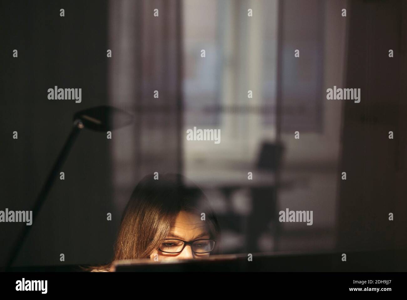 Businesswoman wearing eyeglasses using computer seen through glass at office Stock Photo