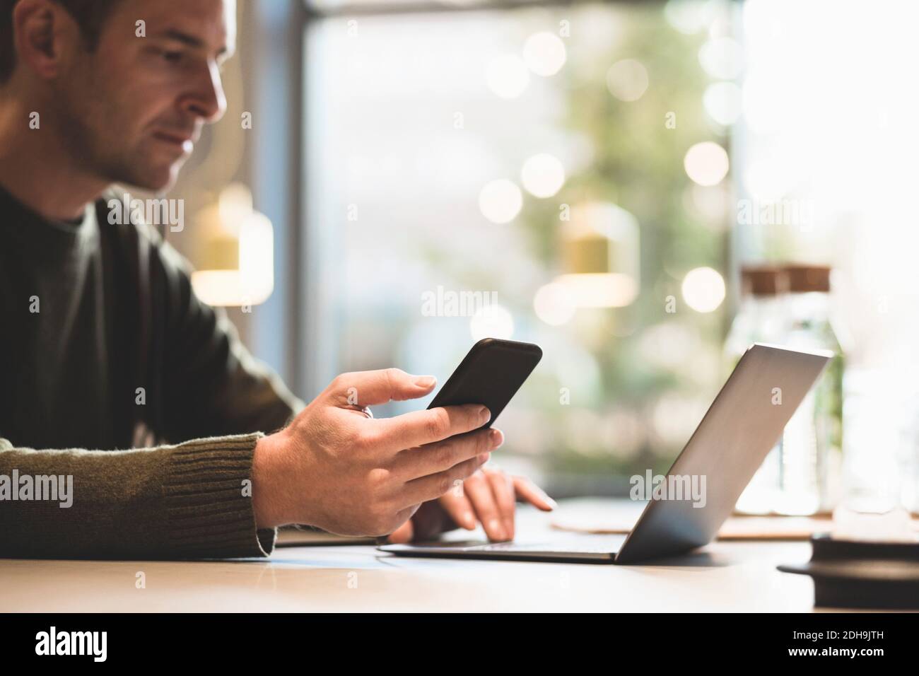 Serious businessman using mobile phone while using laptop at table in office Stock Photo