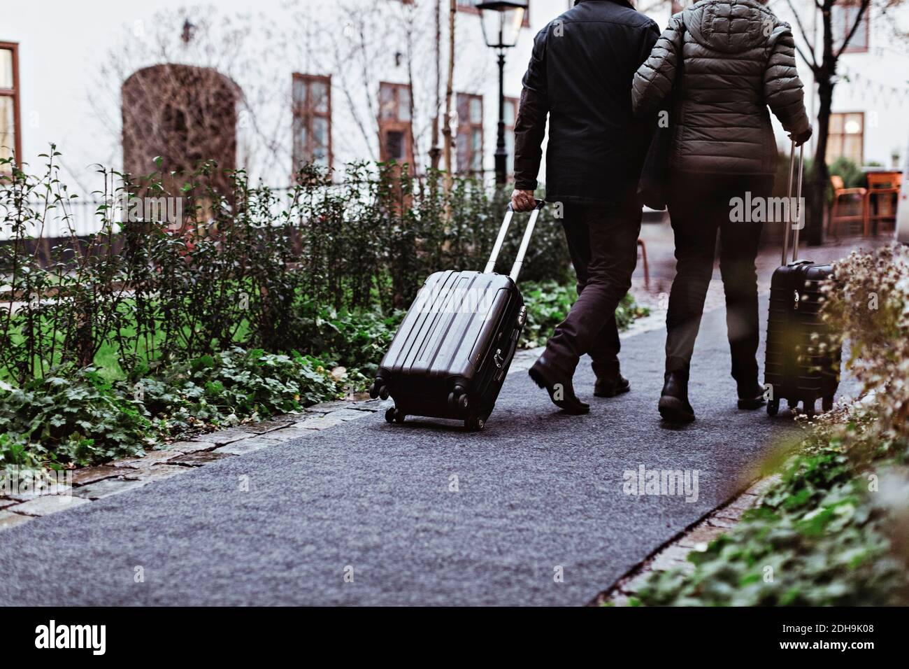 Rear view of senior couple walking on footpath with luggage outside hotel Stock Photo