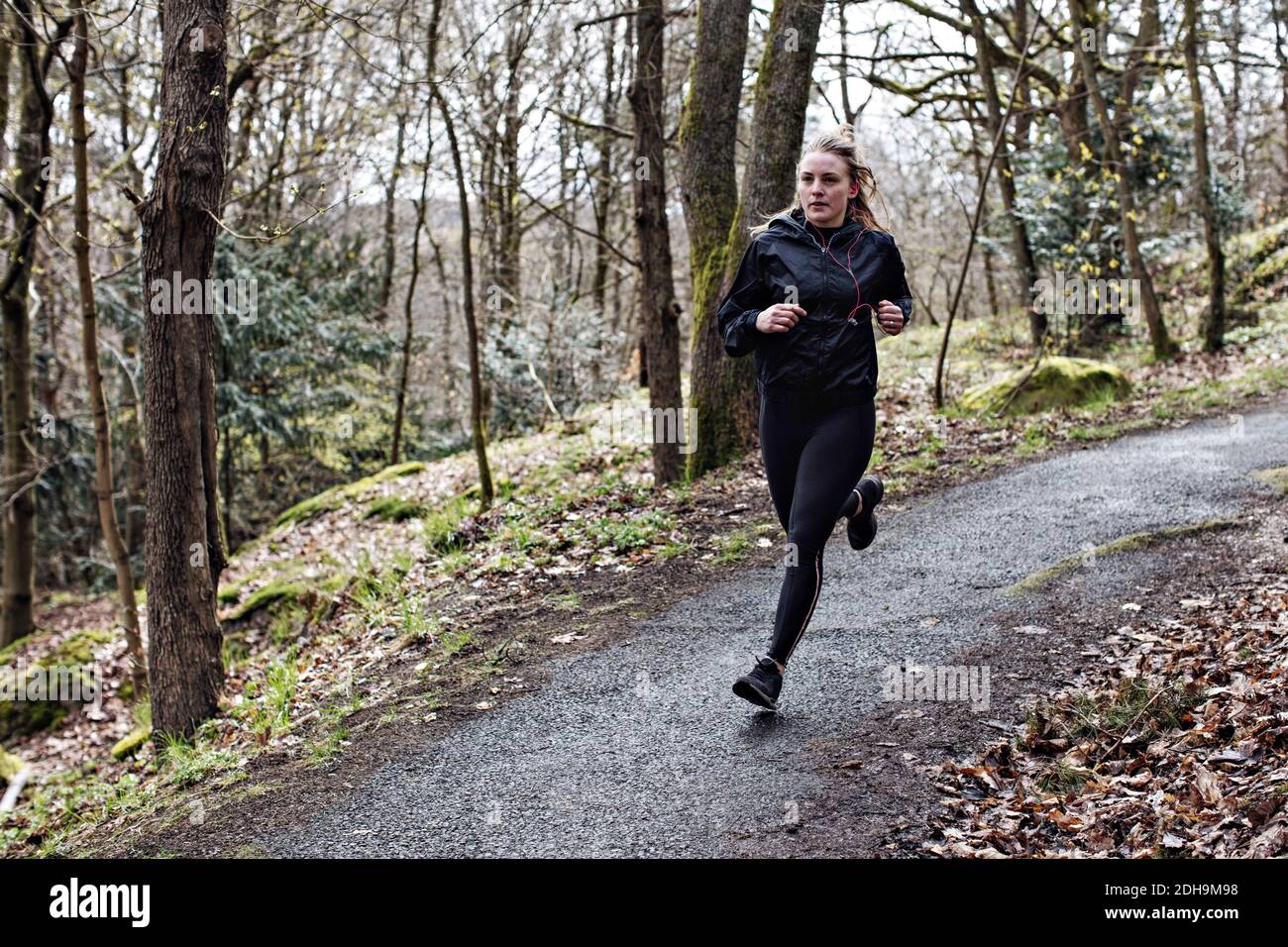 Full length determined female athlete running on narrow road in forest Stock Photo
