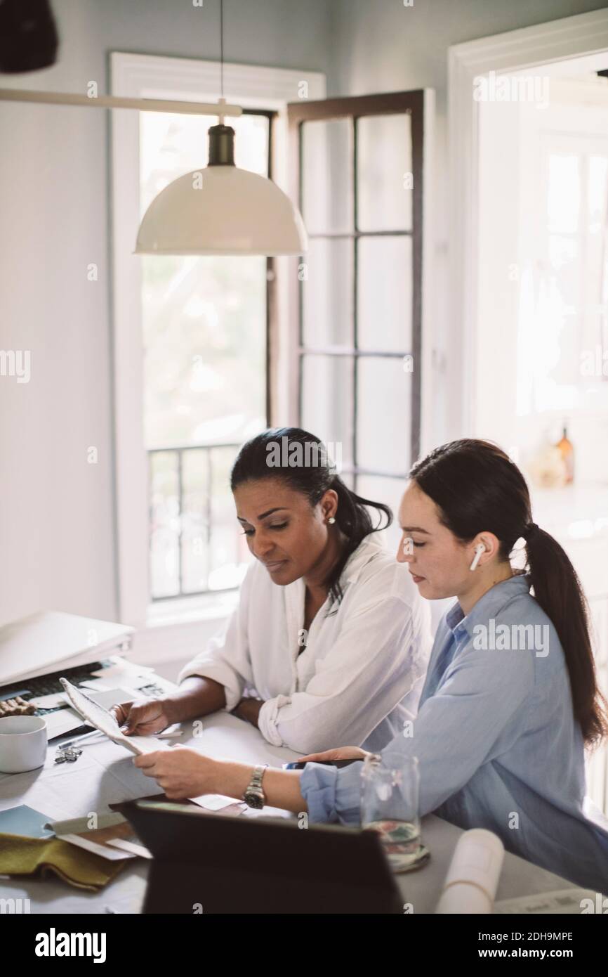 Side view of architect discussing with coworker while working at table in home office Stock Photo