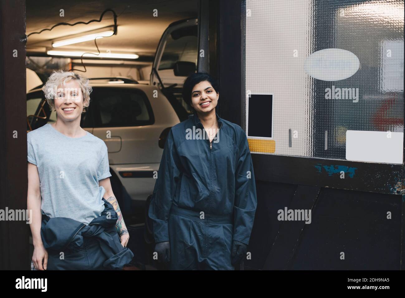 Portrait of smiling female mechanics standing at doorway of auto repair shop Stock Photo