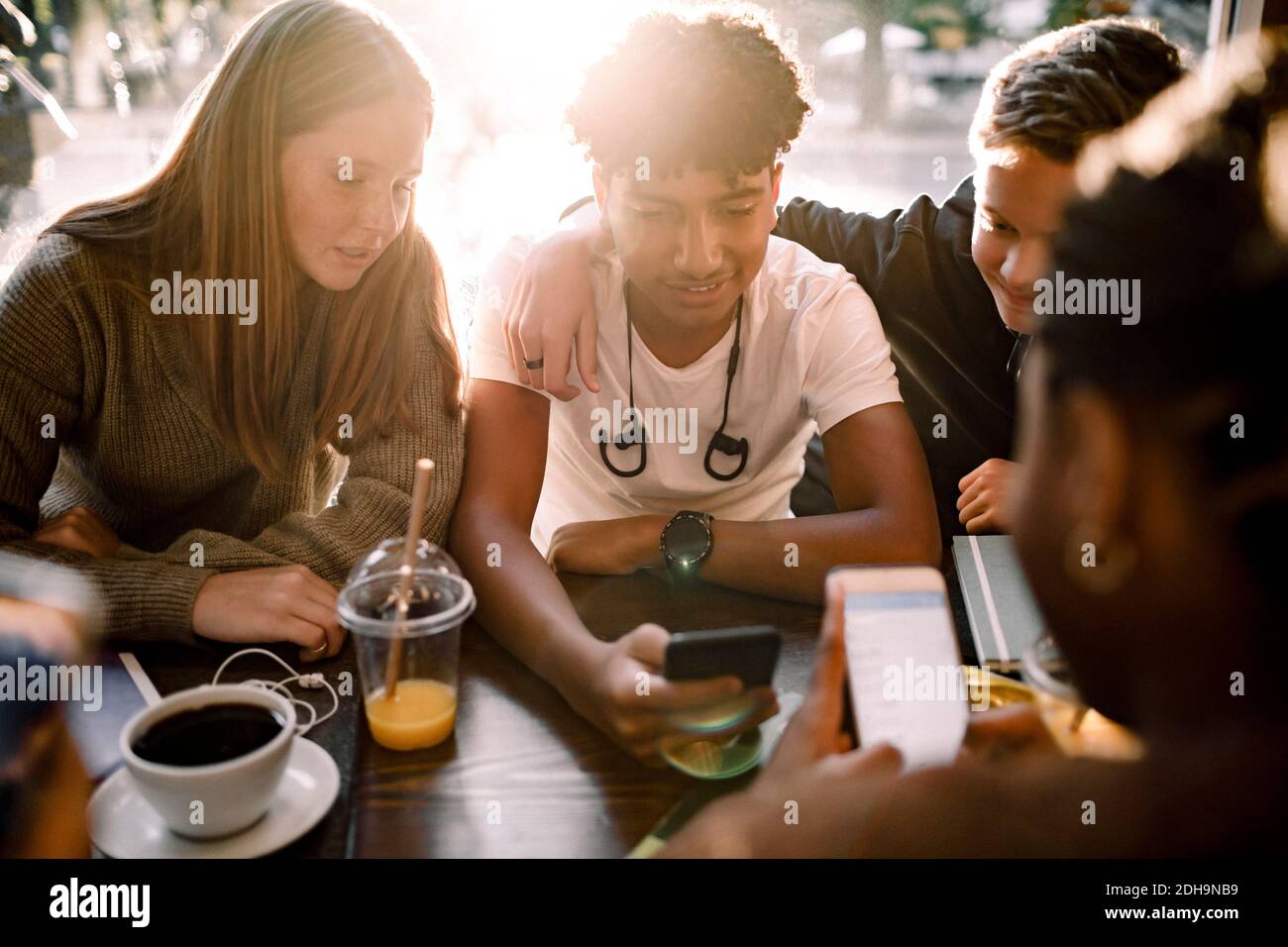Teenage girls and boys surfing internet on mobile phones while sitting in cafe Stock Photo
