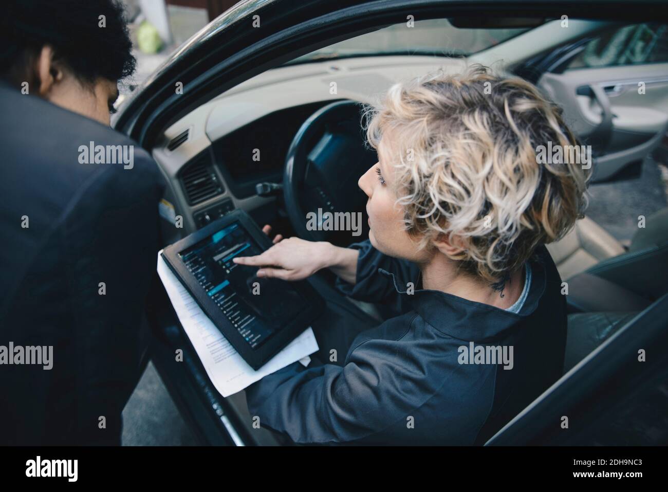 Female mechanic explaining customer over digital tablet while sitting in car Stock Photo