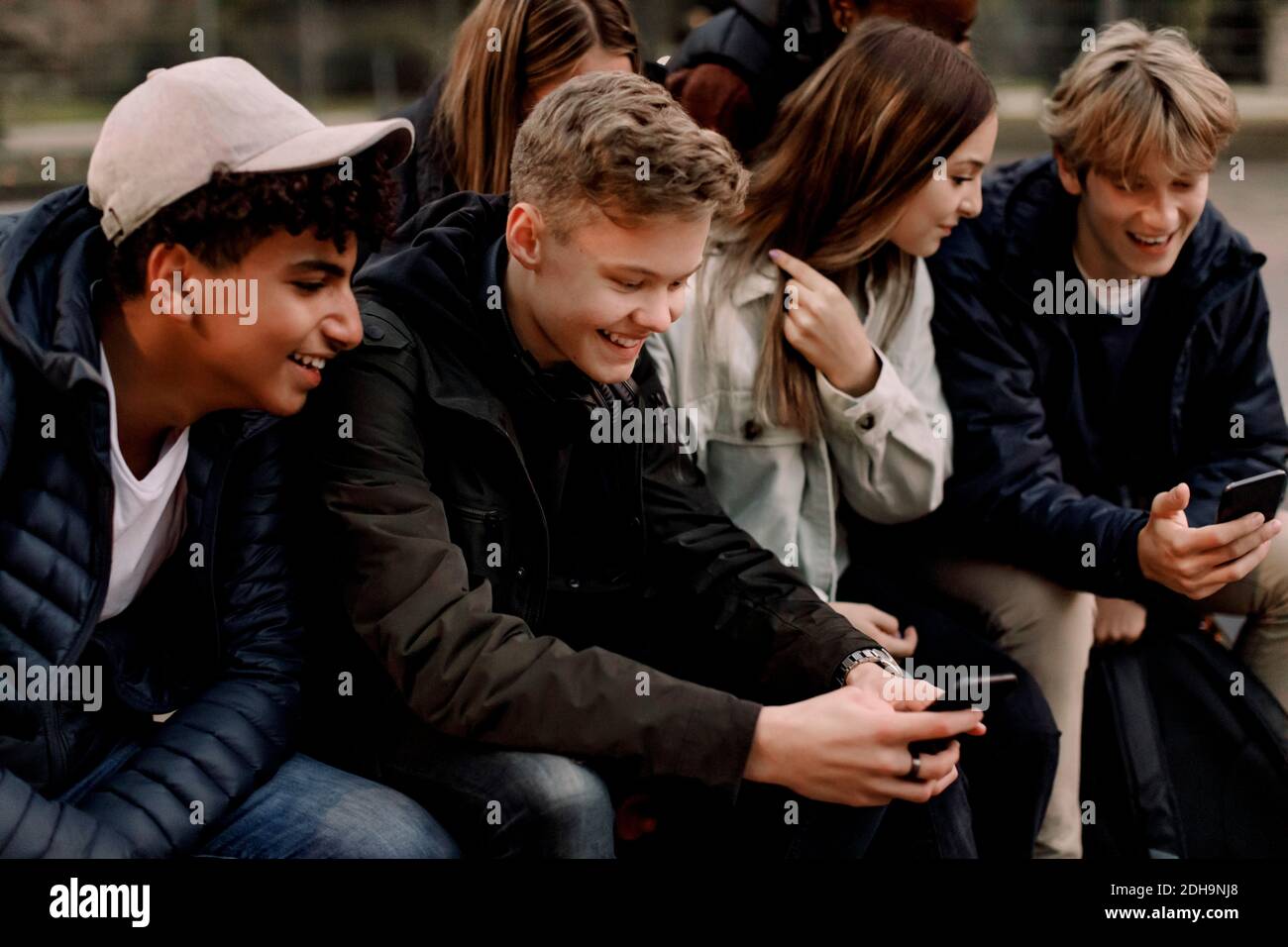 Smiling teenage girls and boys using mobile phones while sitting at park Stock Photo