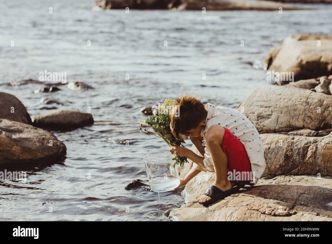 Boy crouching over rock while filling water in container during weekend Stock Photo
