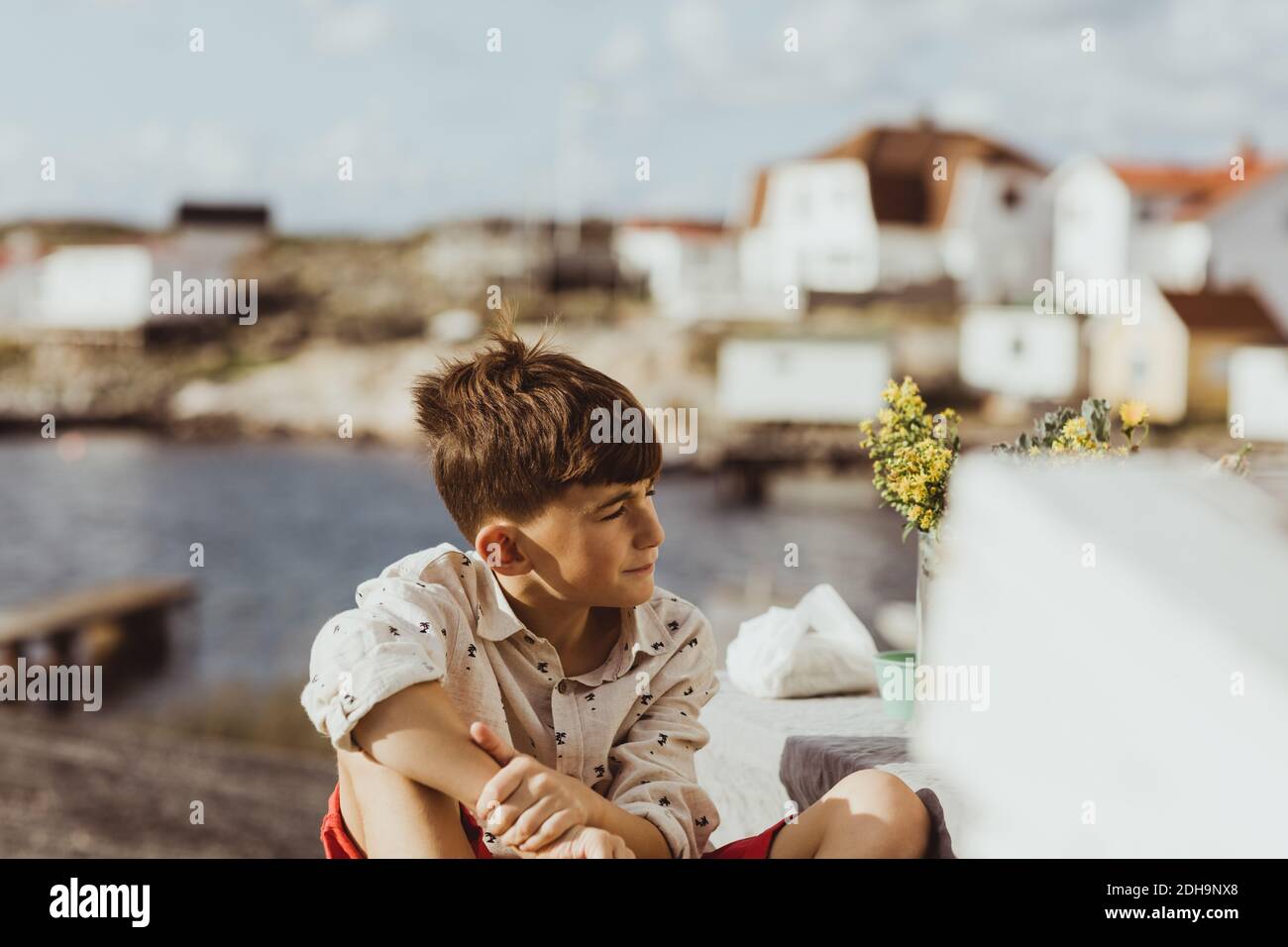 Contemplating boy looking away while sitting outdoors during sunny day Stock Photo