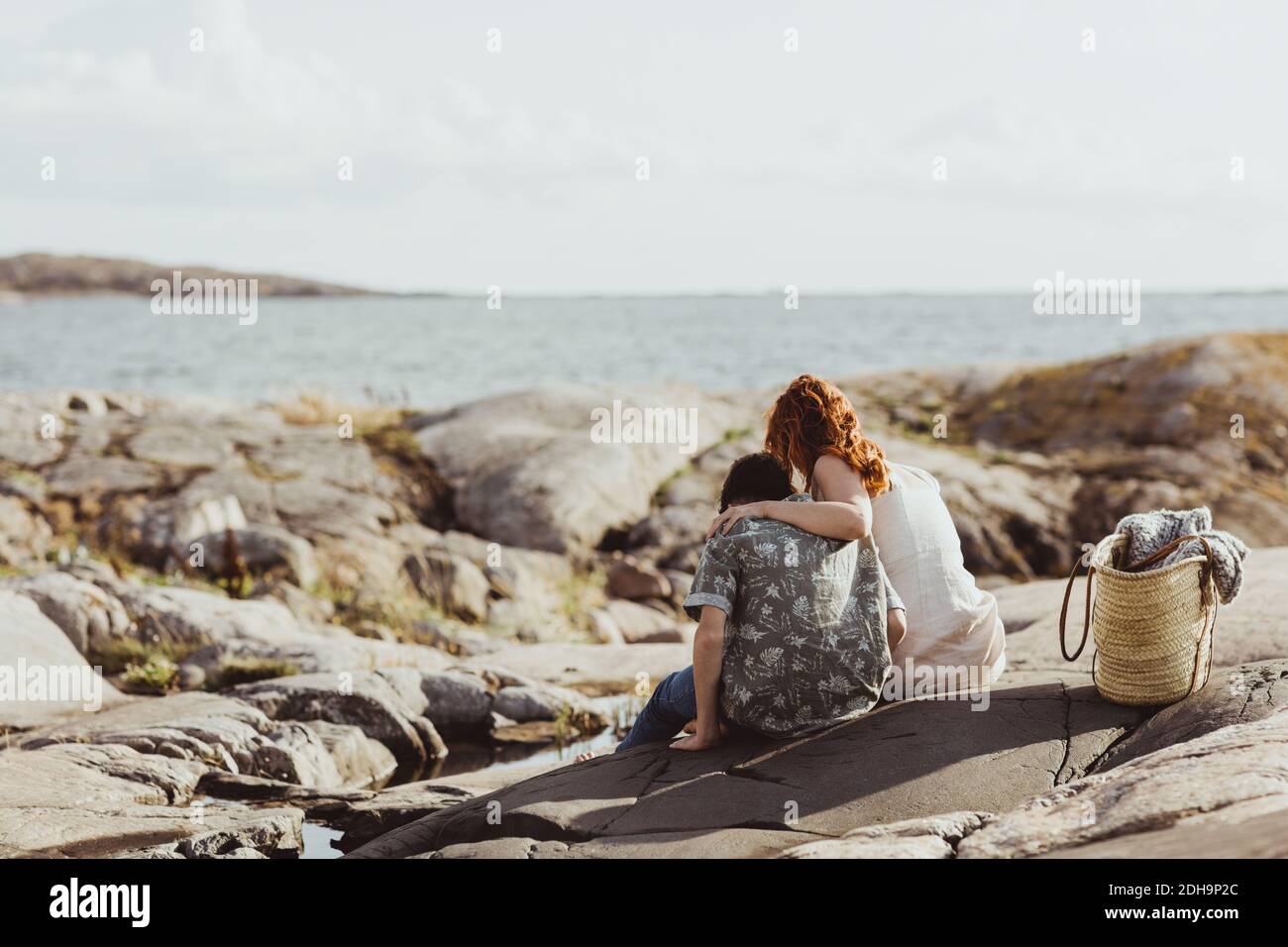 Rear view of mother and son bonding while sitting over rocky land during sunny day Stock Photo