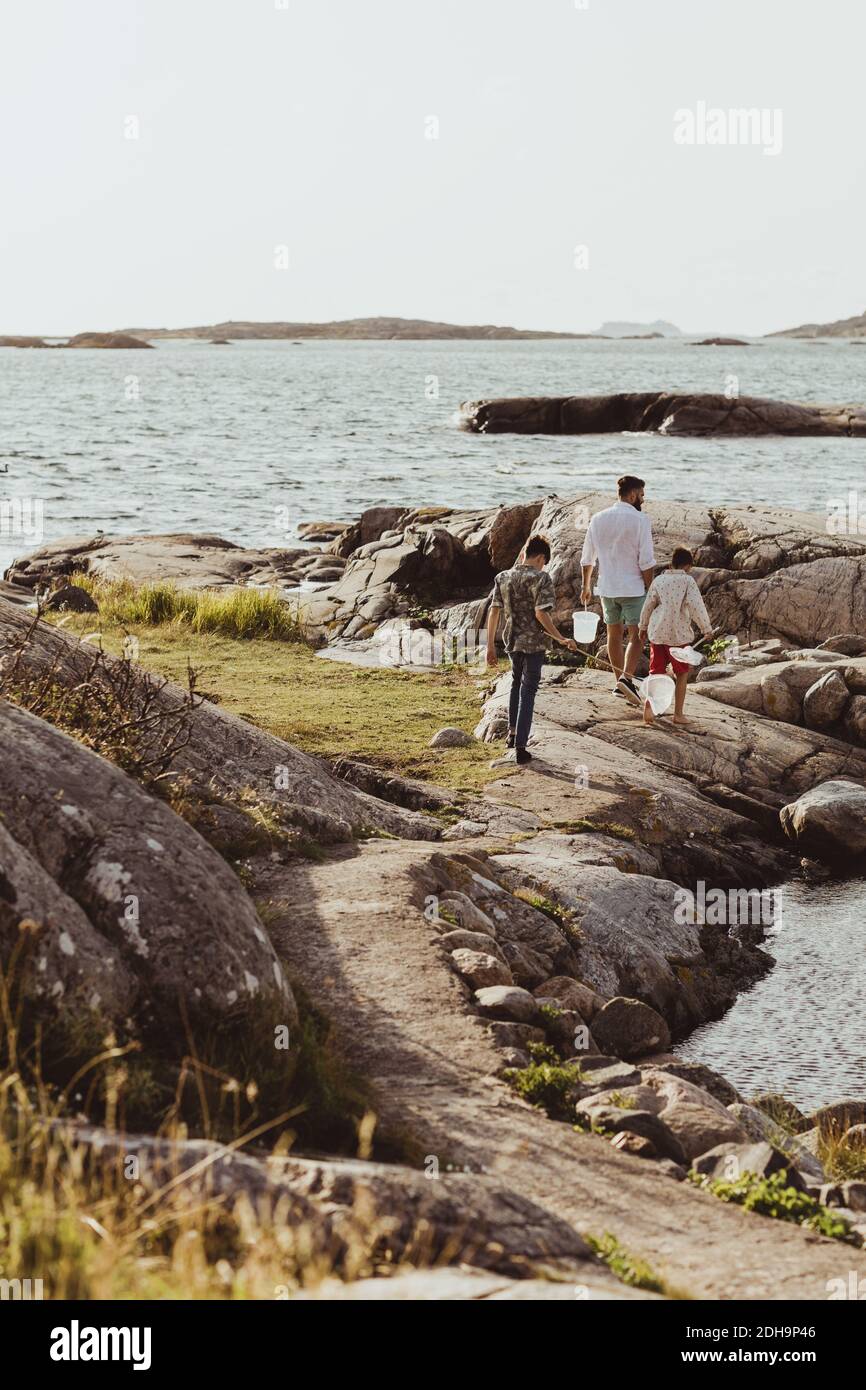 Rear view of teenage boy with sibling walking by father over rocky land during weekend Stock Photo