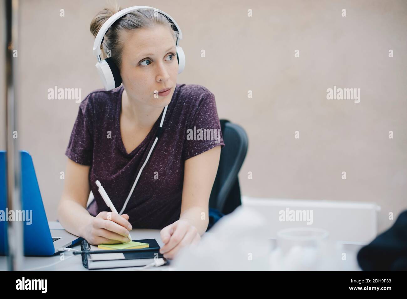 Female computer programmer looking away while writing on adhesive note in office Stock Photo