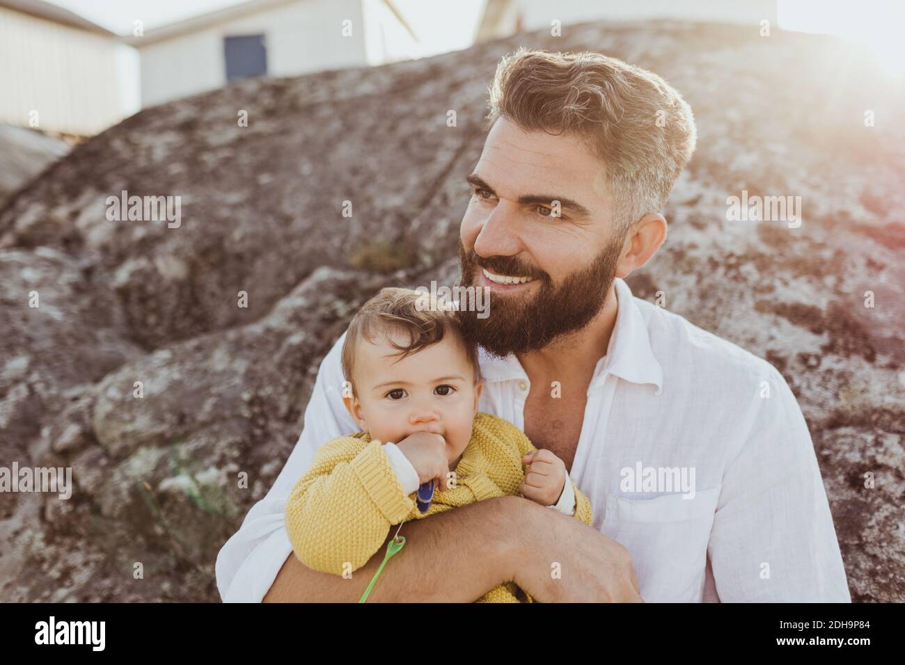 Portrait of baby girl with father looking away while sitting on rock formation Stock Photo
