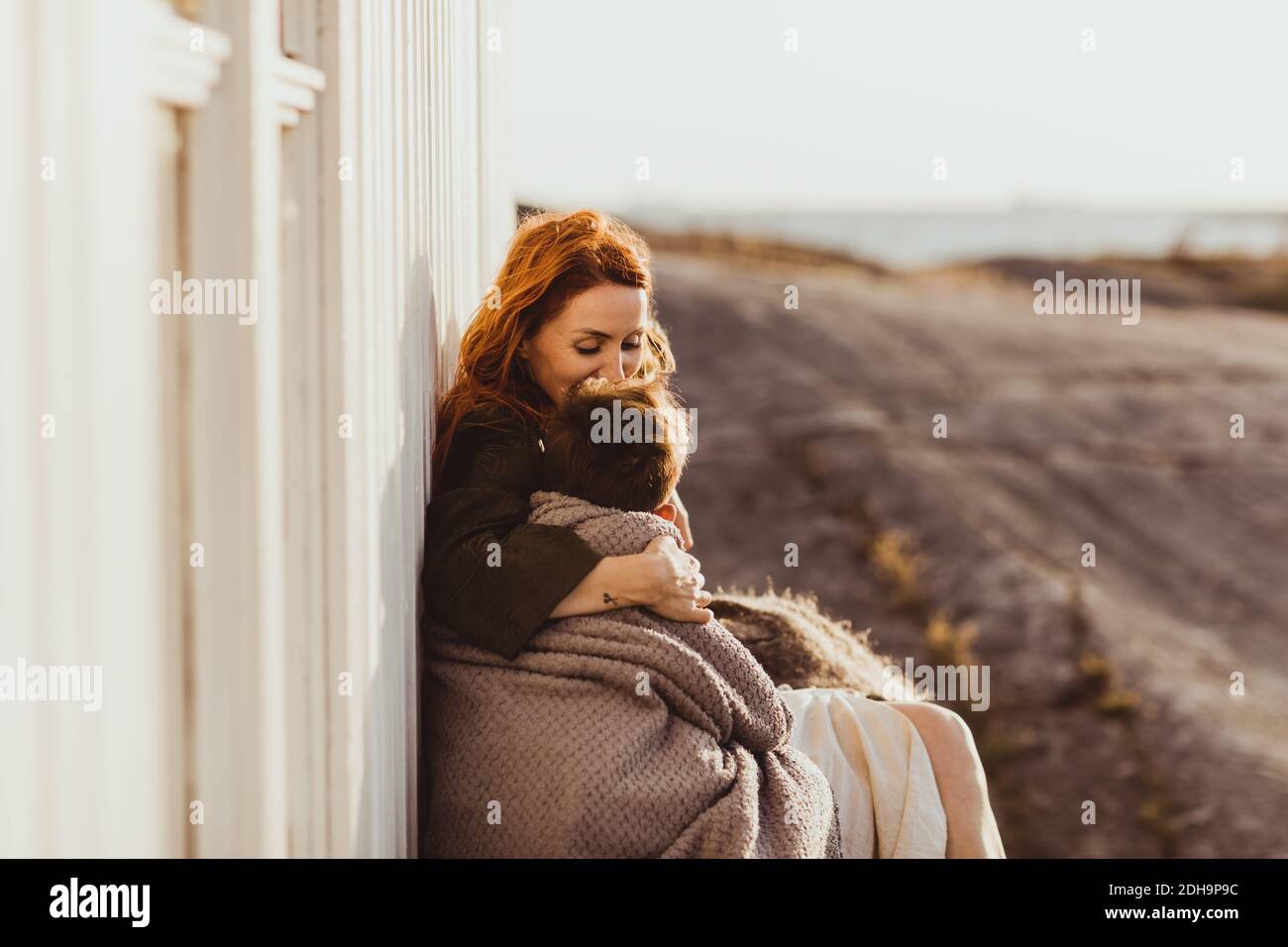 Mother kissing while sitting with son by built structure Stock Photo