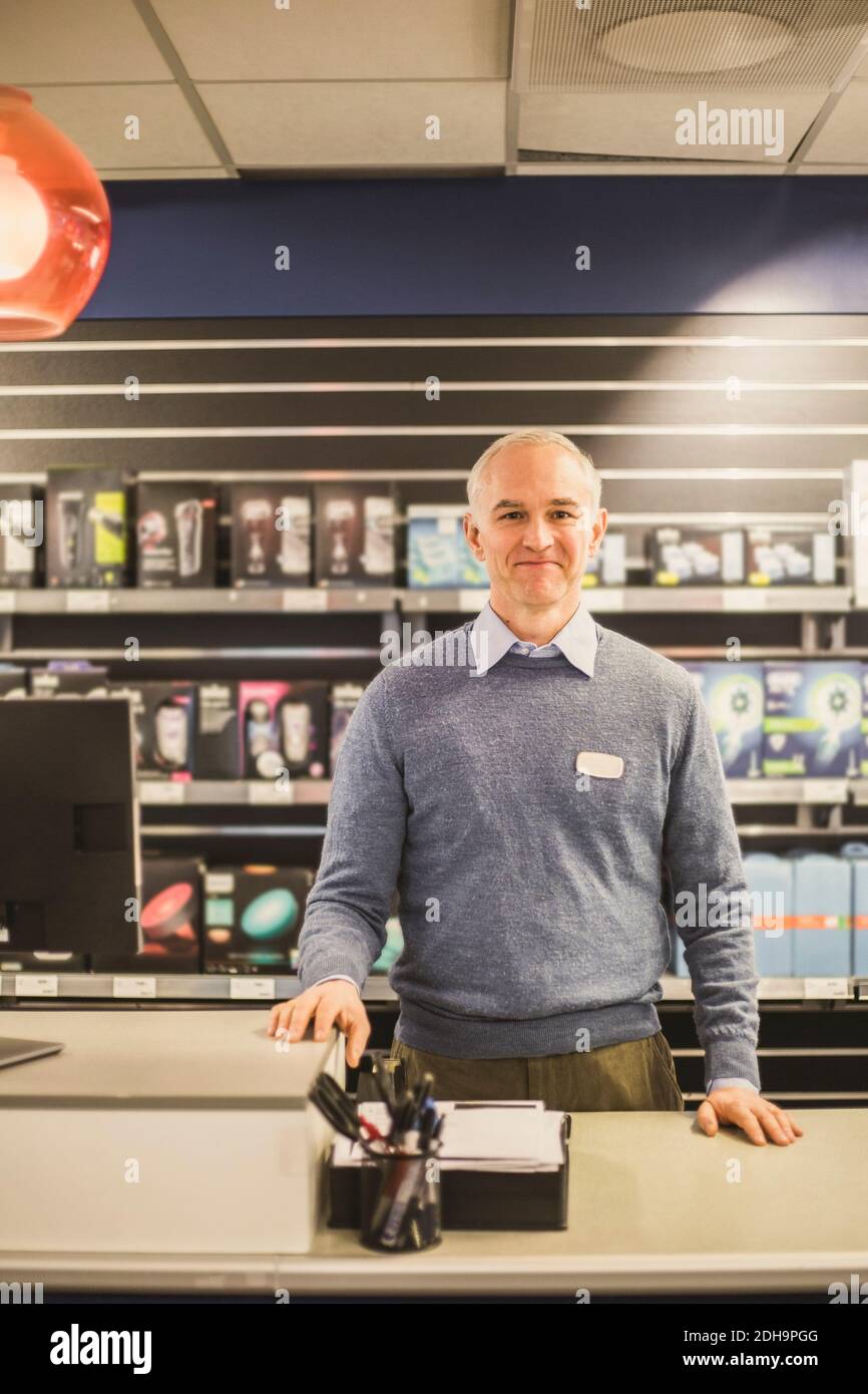 Portrait of smiling mature salesman standing in electronics store Stock Photo