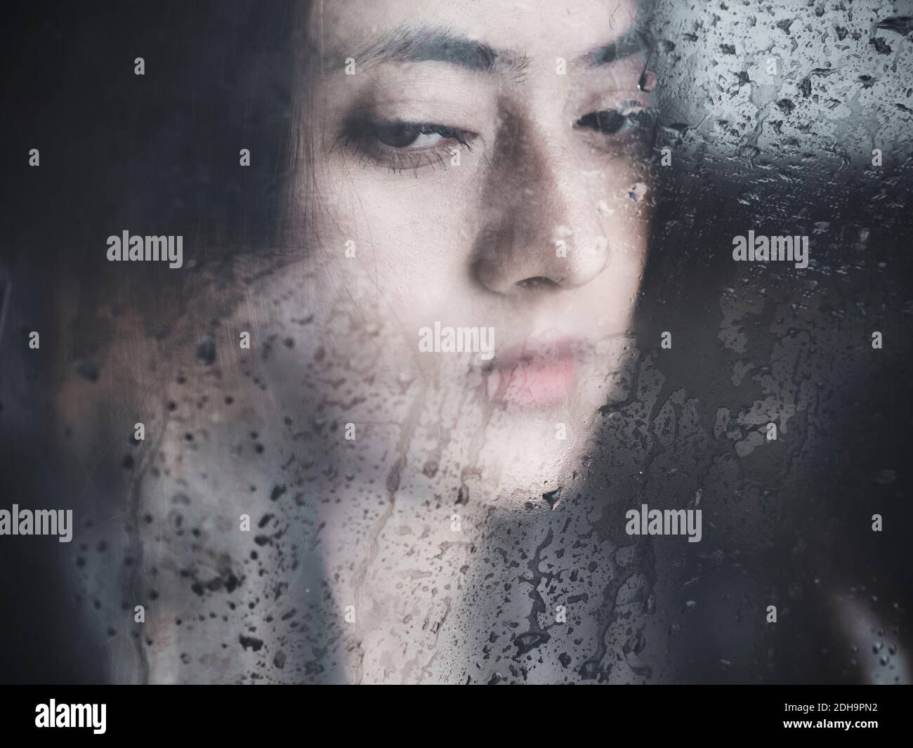 Pensive young Nepalese woman behind wet glass Stock Photo