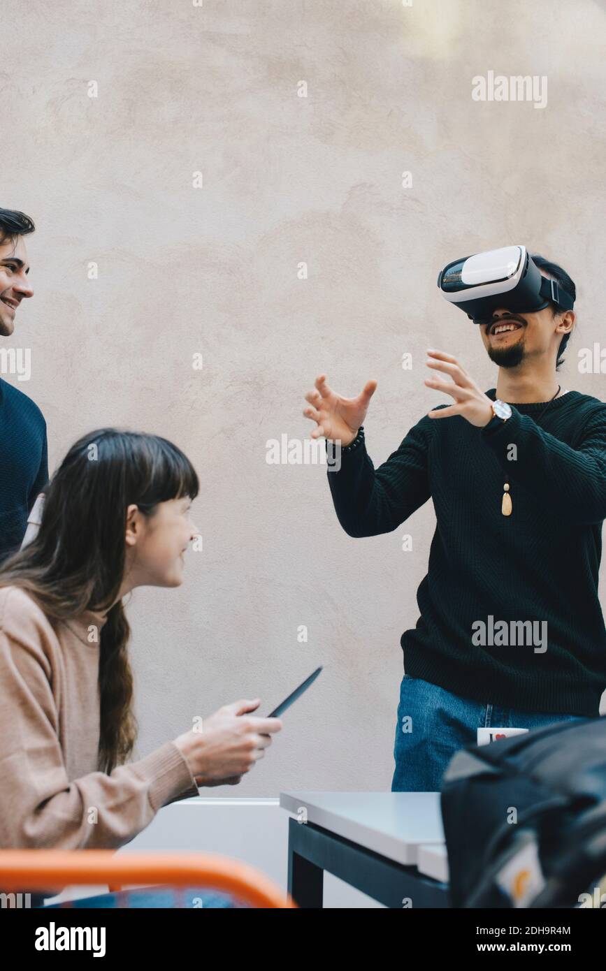 Smiling male computer programmer gesturing while using VR glasses by colleagues in office Stock Photo