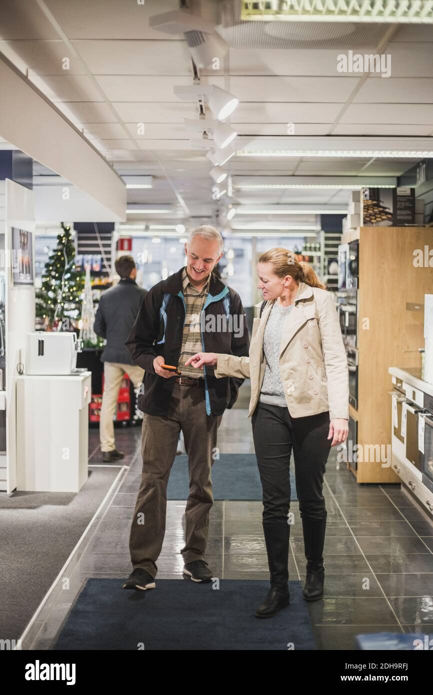 Mature friends talking over smart phone while standing in electronics store Stock Photo