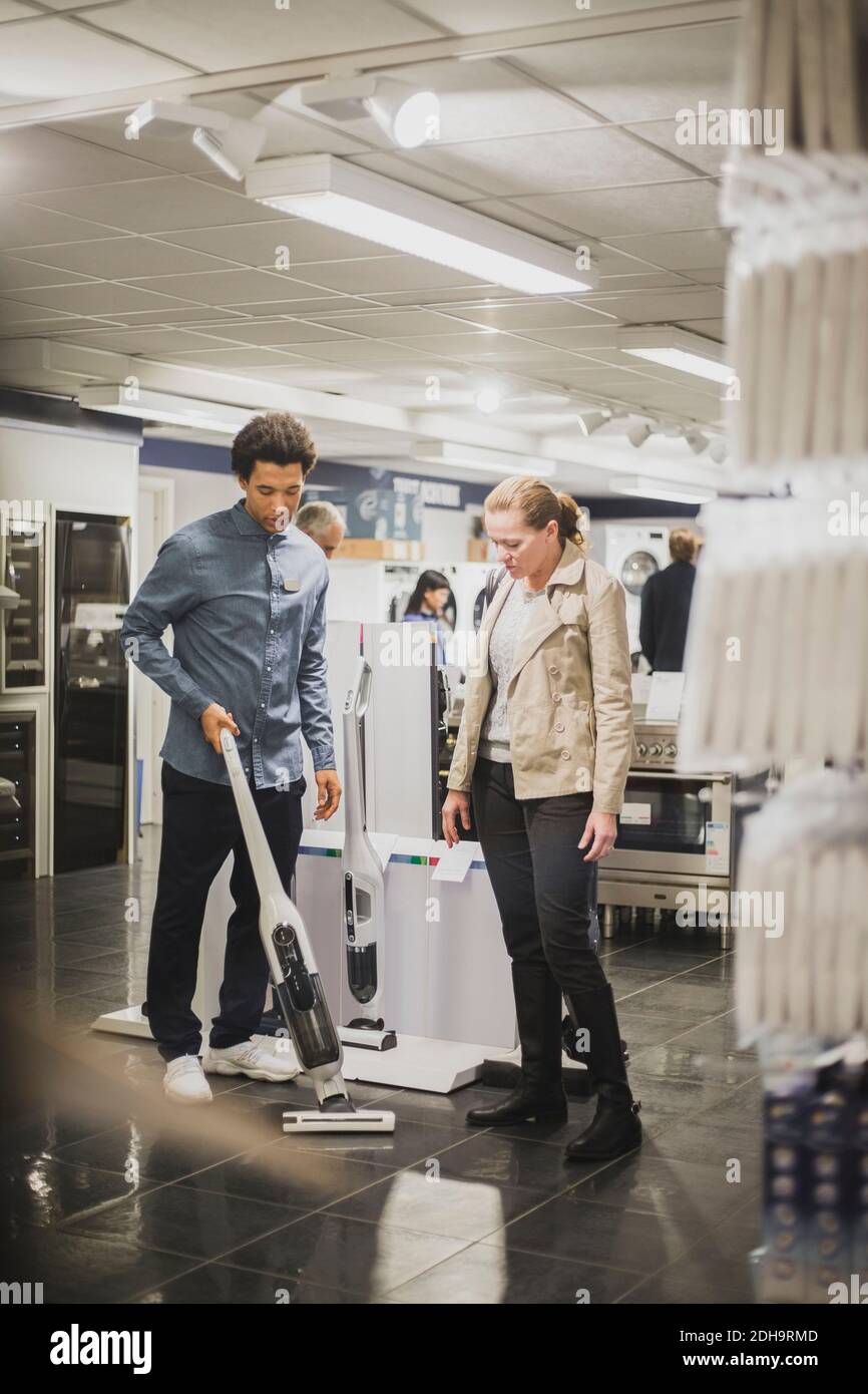Salesman showing cleaning equipment to female customer in electronics