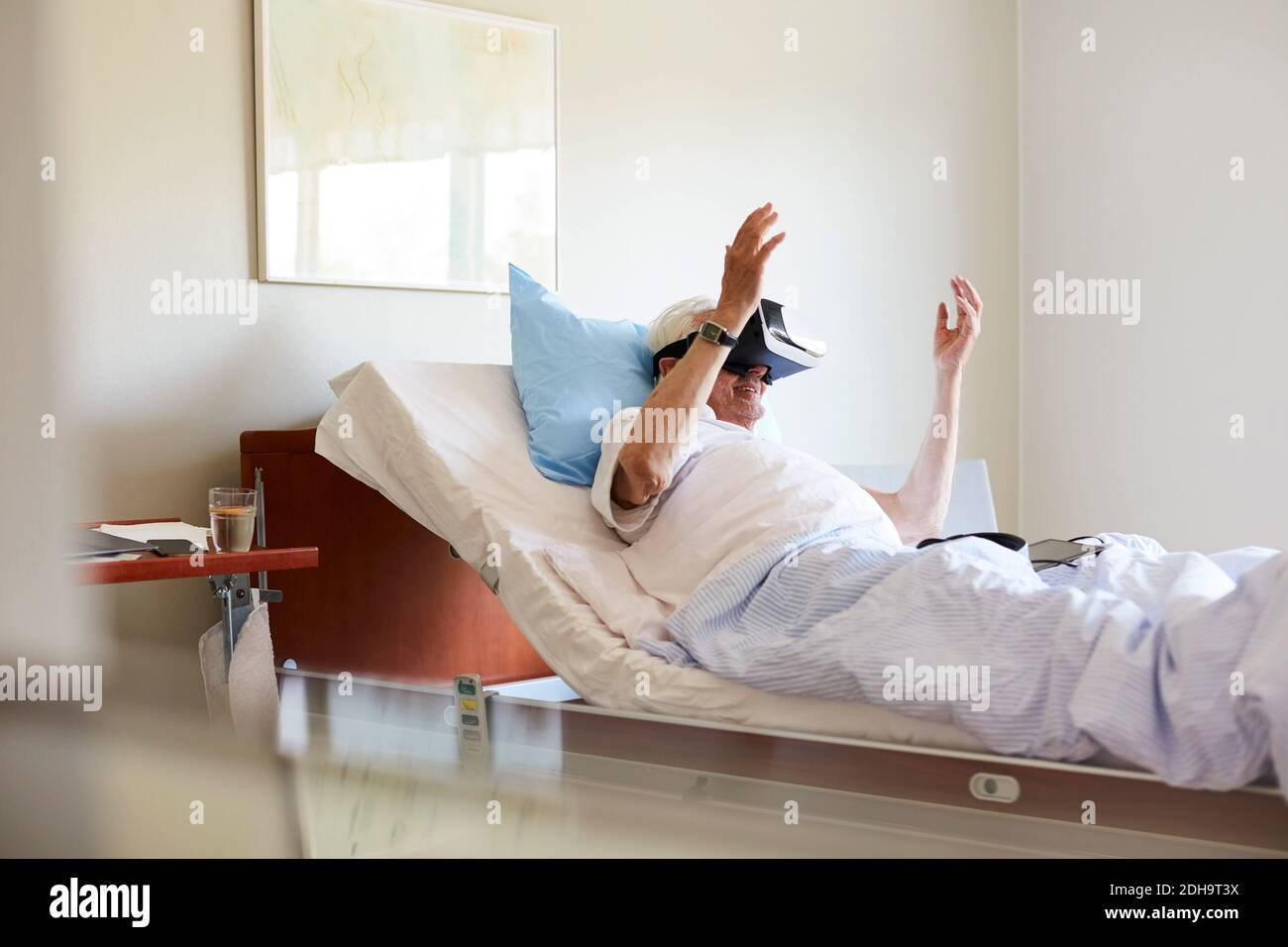 Senior man using VR glasses on bed in hospital ward Stock Photo