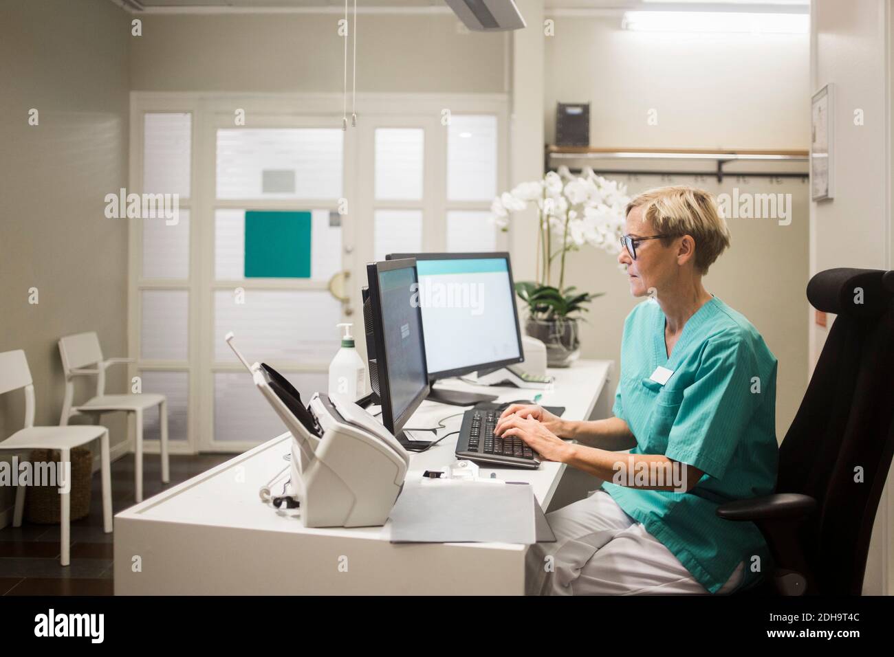 Side view of mature female doctor working over computer while sitting in clinic Stock Photo