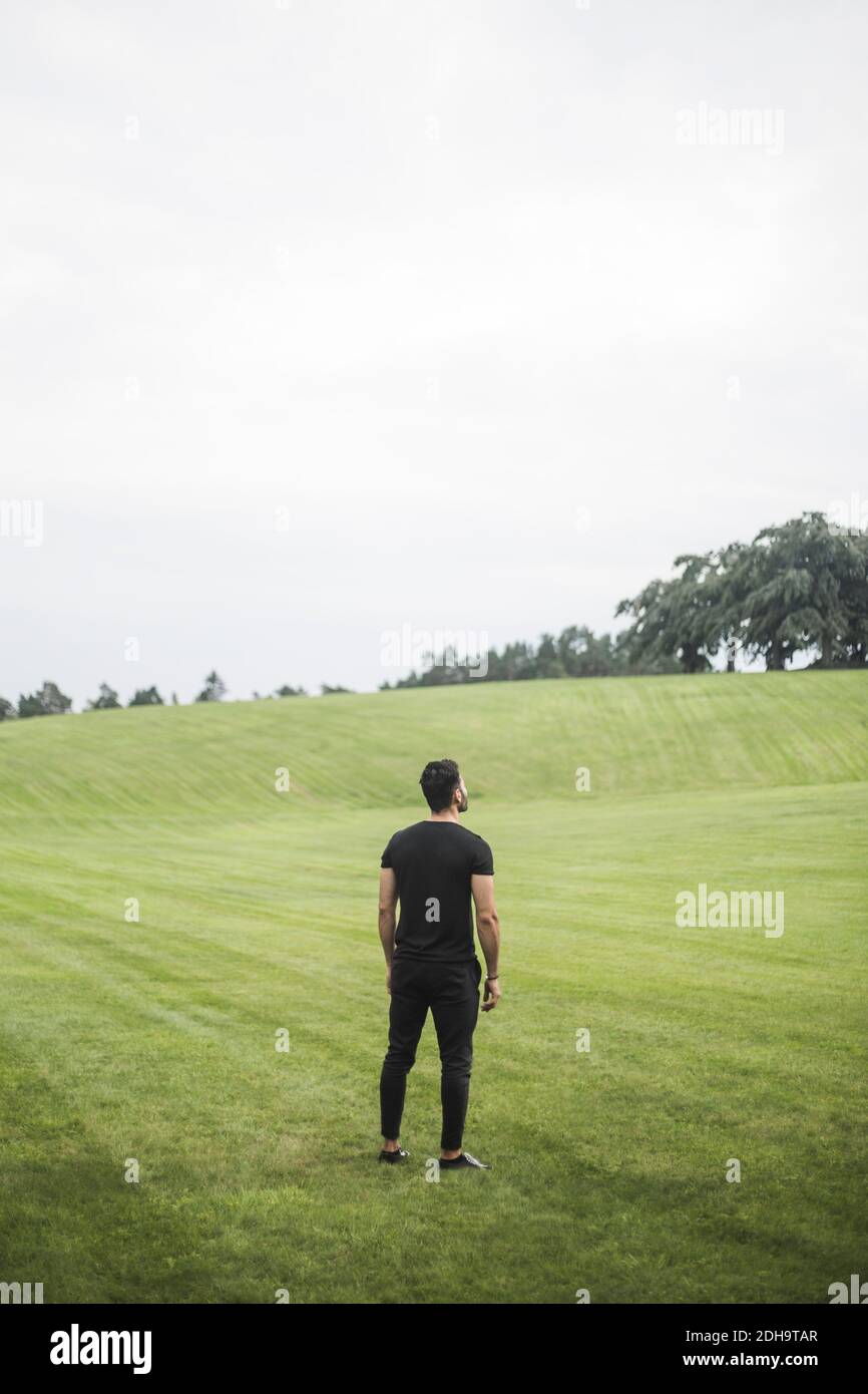 Rear view of young man standing on agricultural field against sky Stock Photo
