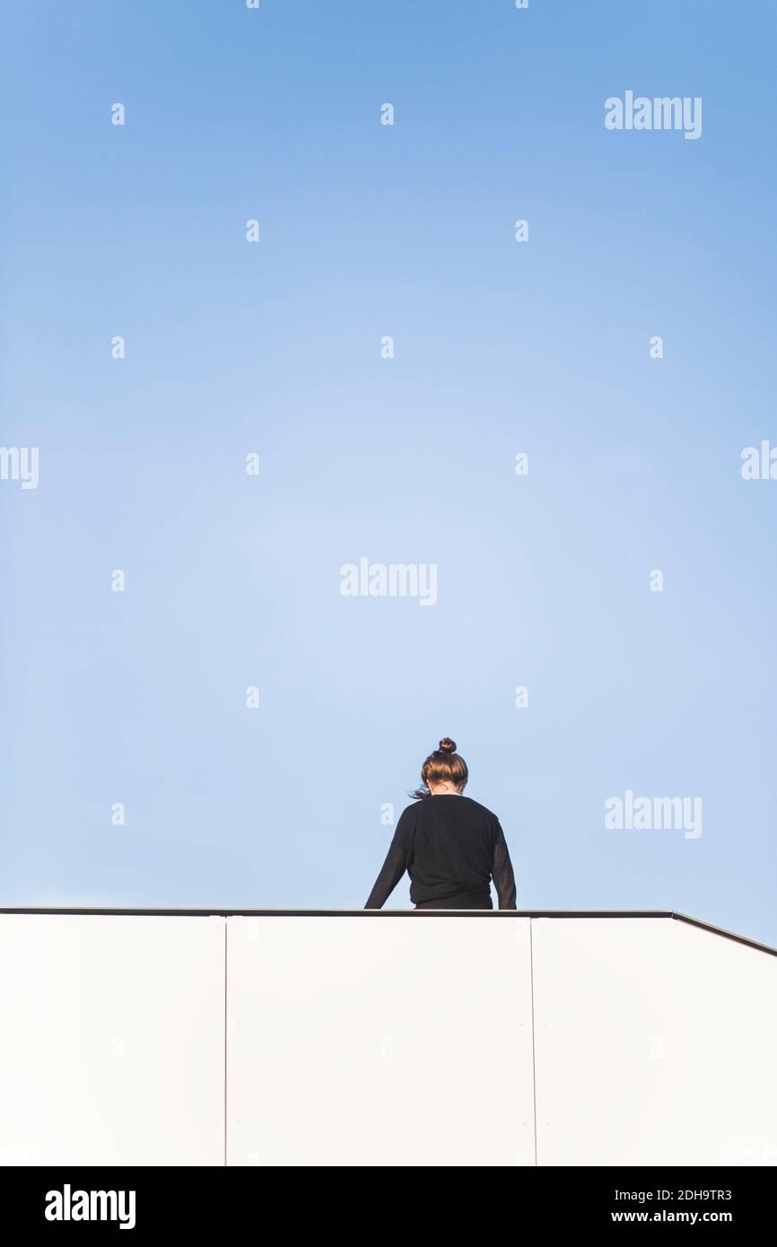 Rear view of woman standing by built structure against blue sky Stock Photo
