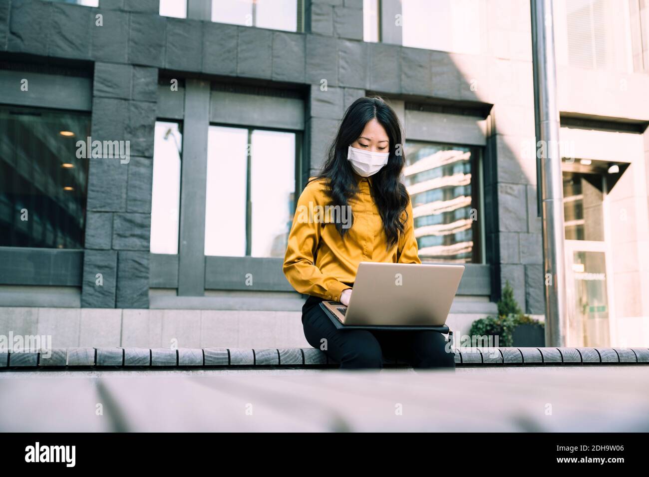 Businesswoman with face mask working using laptop Stock Photo