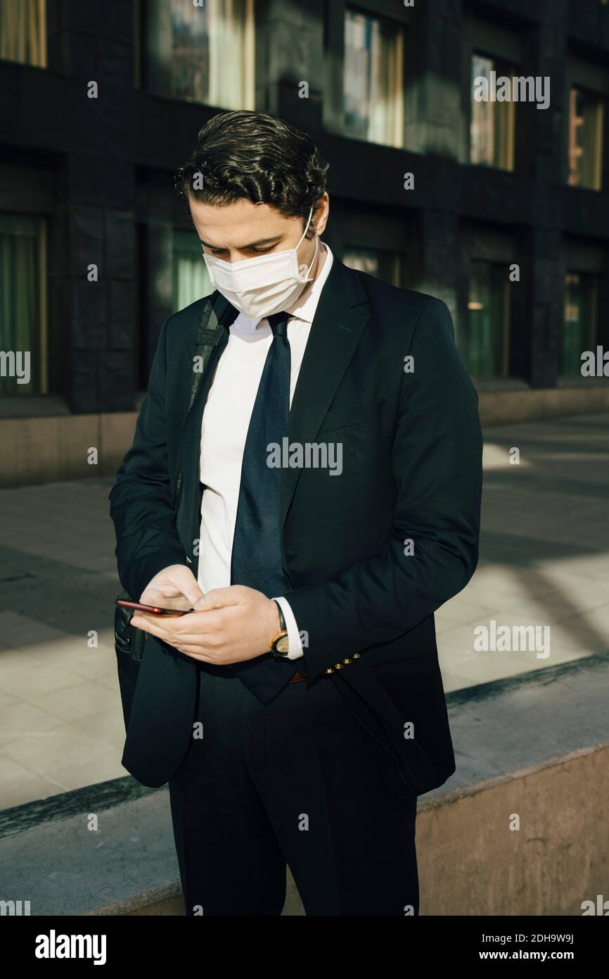 Businessman with face mask using smartphone Stock Photo