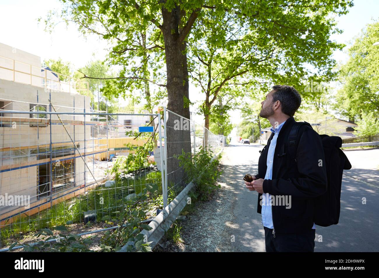 Businessman looking at incomplete building while standing on street during sunny day Stock Photo