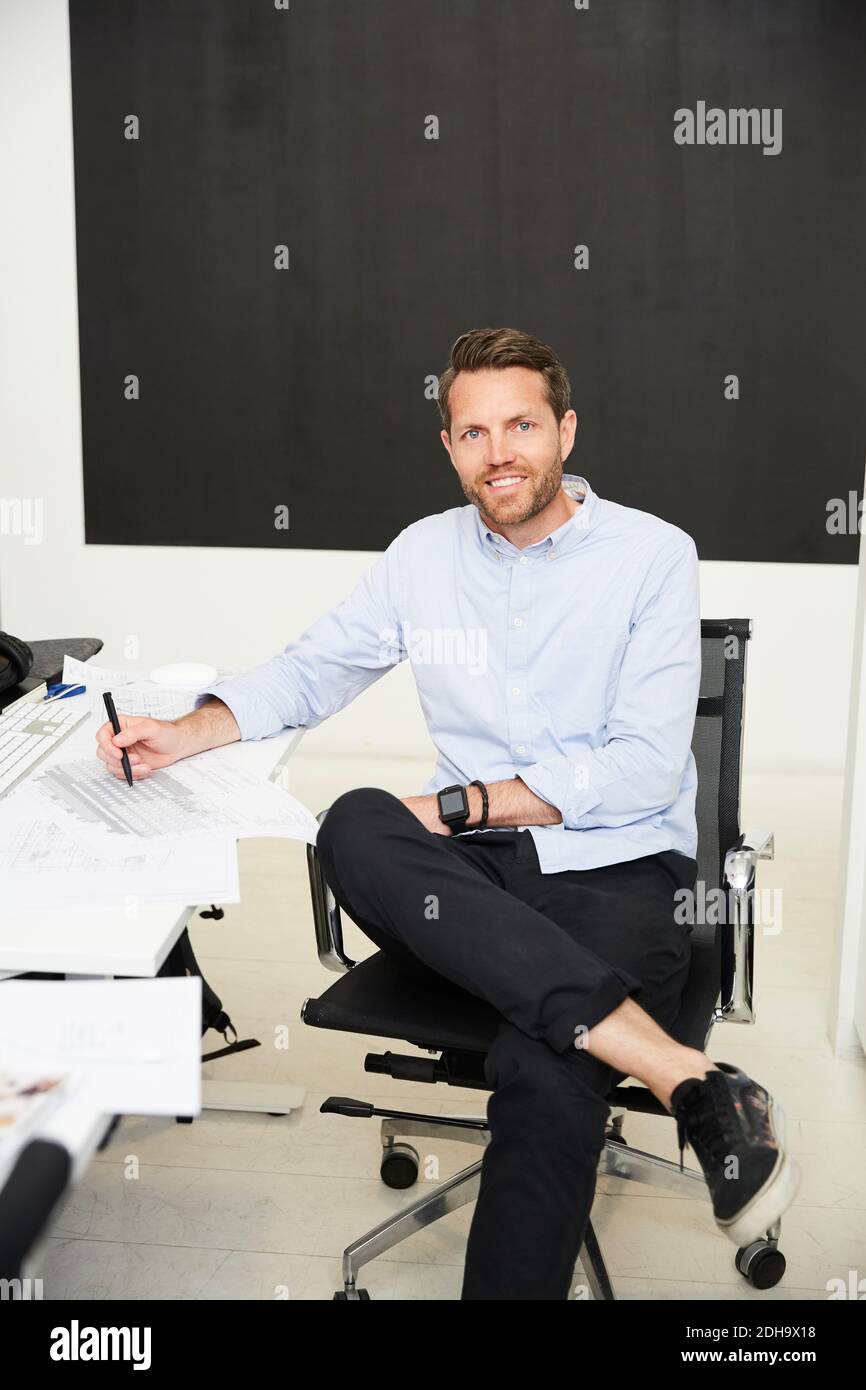 Portrait of confident architect with blueprints in creative office Stock Photo