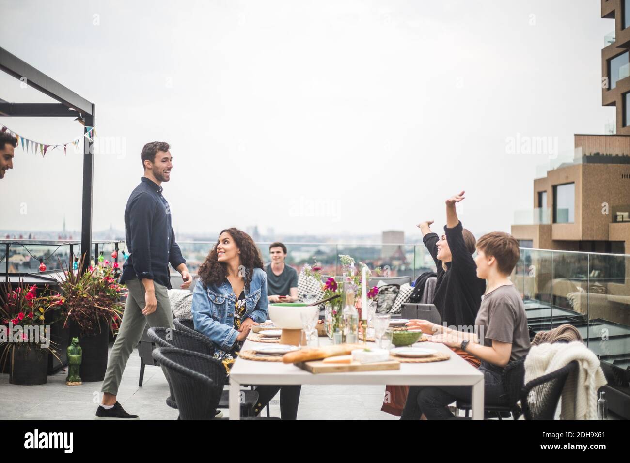 Young female with arms raised greeting friends while sitting by table on terrace Stock Photo
