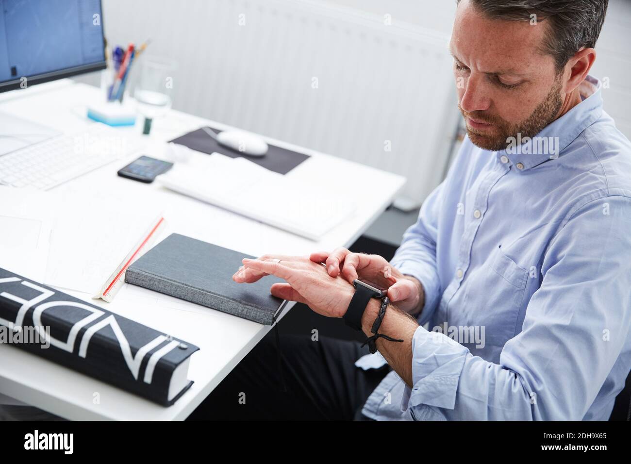 Businessman checking time while sitting at desk in creative office Stock Photo