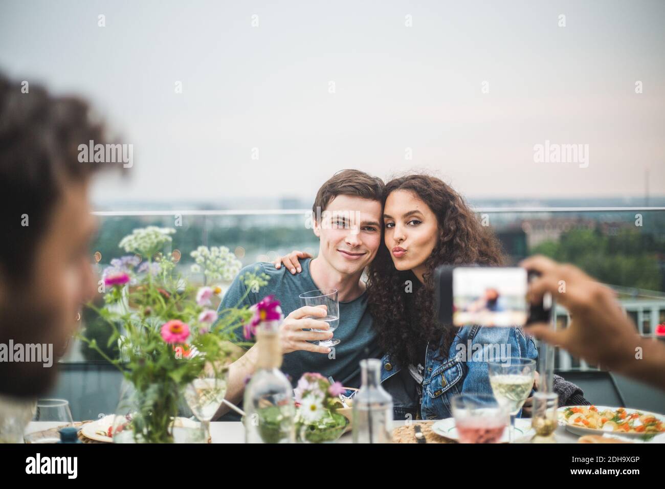 Cropped hand of man clicking photograph of couple through phone on terrace during party Stock Photo